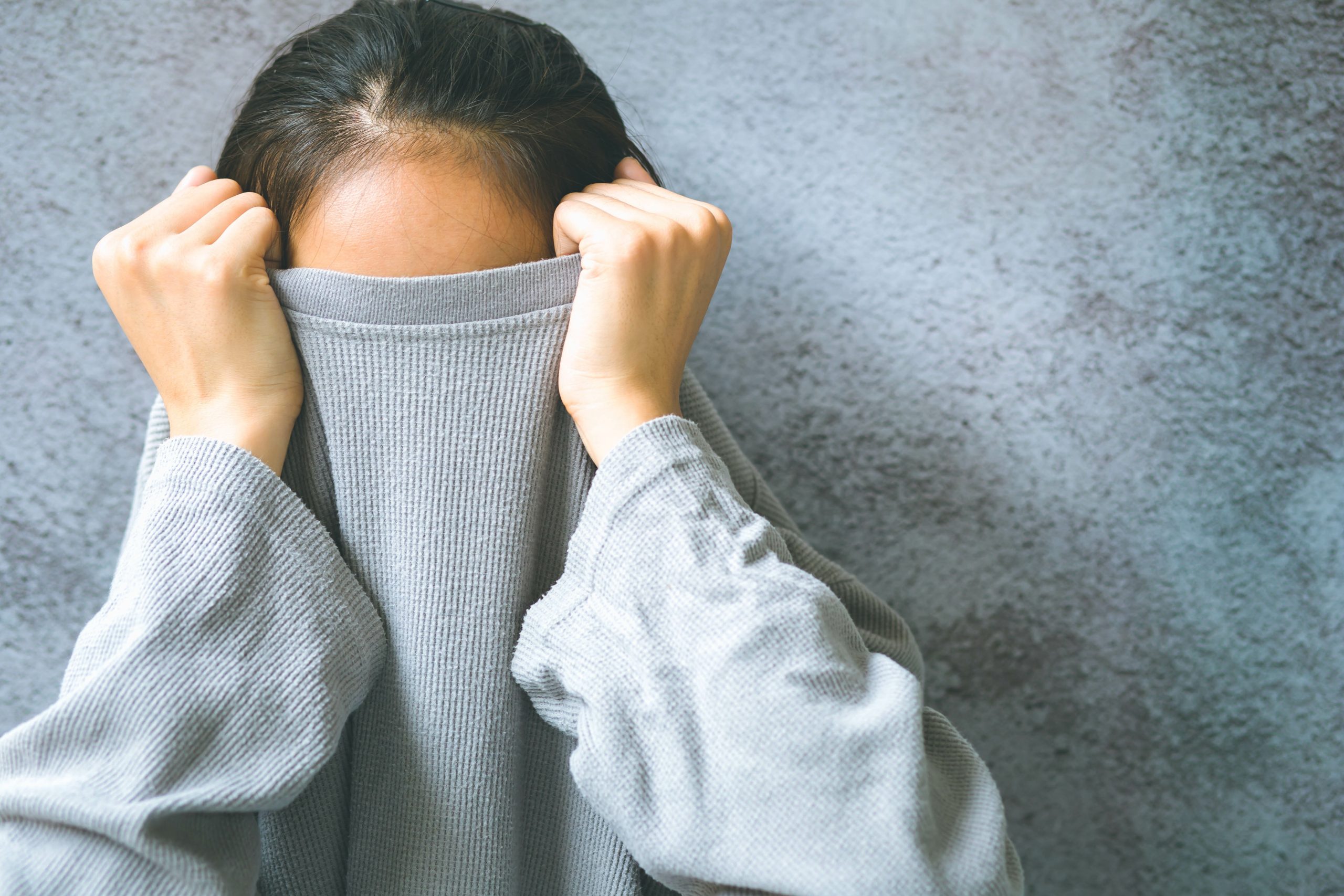 Asian woman hiding face under the clothes. She is oulling sweate Counselling and Psychotherapy services in Antrim - NI Counselling